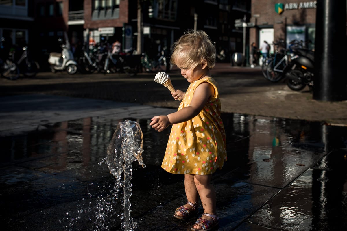 Meisje speelt bij een fontein terwijl haar ijsje bijna valt