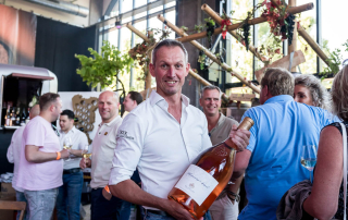 De barman toont een hele grote fles rose tijdens het wijnfestival aan de evenementenfotograaf